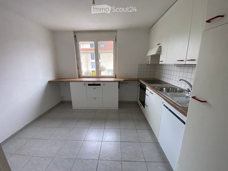 Empty kitchen with white cabinets, tiled floor, and a window overlooking a building.