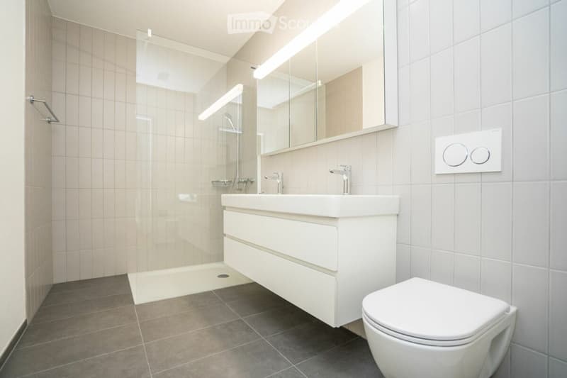 Modern bathroom with white tiles, a white sink with a mirror, a toilet, and a glass-enclosed shower area.
