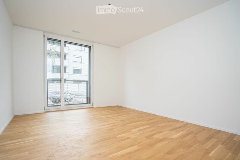 Empty room with light wooden flooring, white walls, and a large glass sliding door leading to a balcony area.