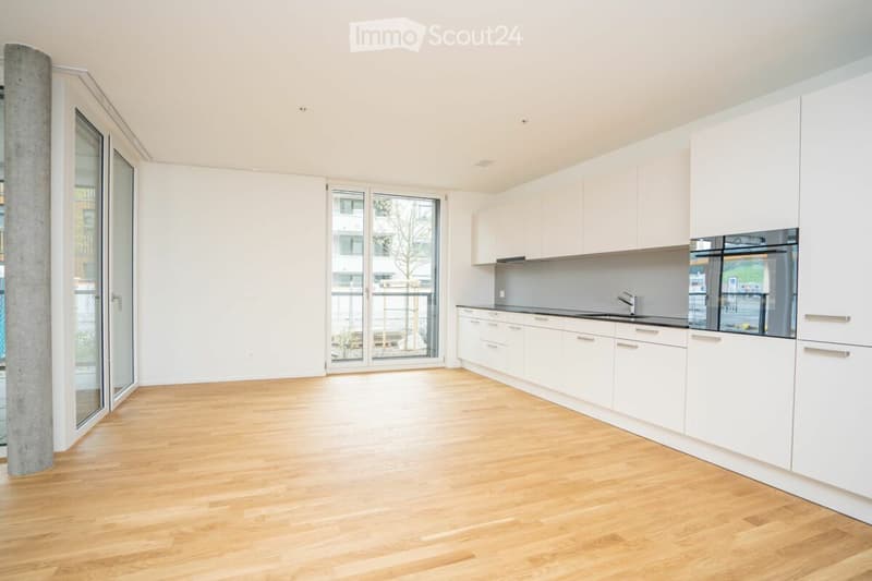 Empty kitchen with white cabinets, wooden flooring, and large windows leading to a balcony.
