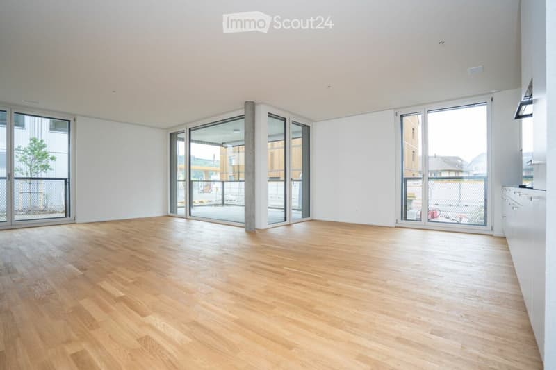 Empty room with light wooden flooring, white walls, and large glass doors leading to an outdoor area.