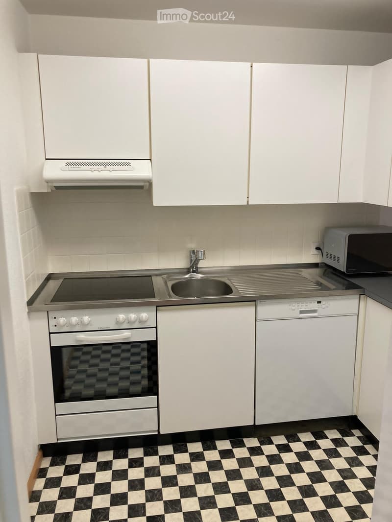 Modern kitchen with white cabinets, stainless steel appliances, and black and white checkered flooring.