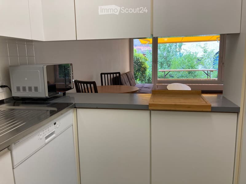 Modern kitchen with white cabinets, microwave, dishwasher, and a small living area with a sofa and table.