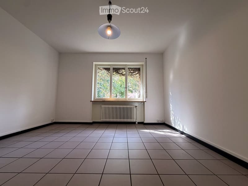 Empty room with tiled floor, white walls, a window with a radiator below, and a hanging light fixture.