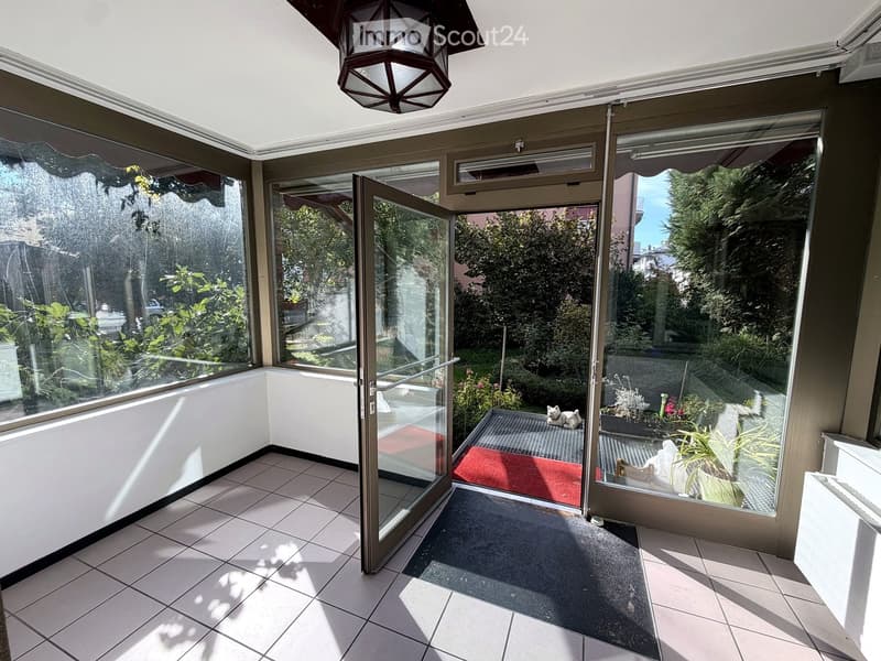 Bright, enclosed balcony with large glass windows and doors, tiled floor, and a hanging lantern light fixture.