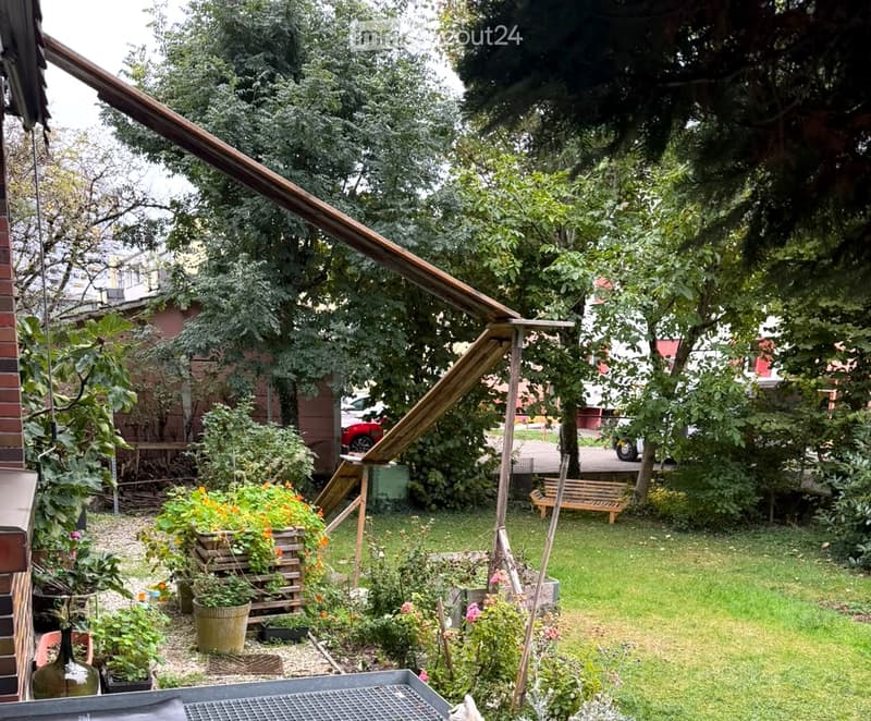 Garden with grass, trees, potted plants, a wooden slide, and a bench.