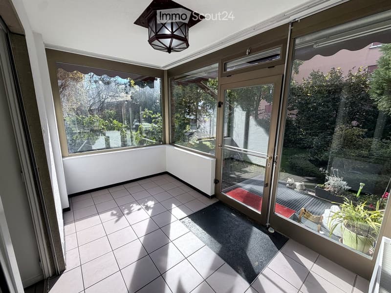 Bright, enclosed balcony with tiled flooring, large glass windows, and a hanging lantern-style light fixture.