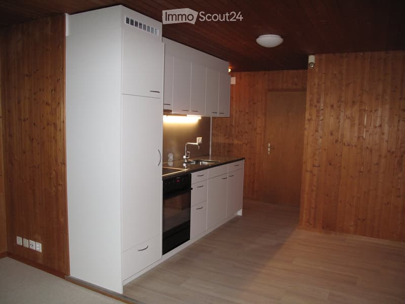 Modern kitchen with white cabinets, wooden walls, and a sleek black oven. The space features a sink with a modern faucet and ample storage in white cabinets.
