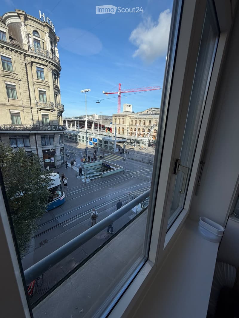 Balcony overlooking a busy urban street with pedestrians, a tram, and historic buildings.