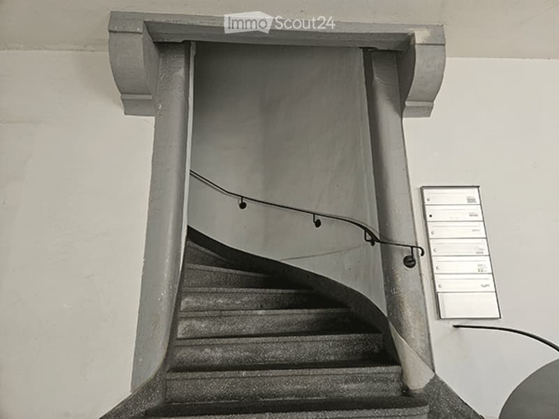 Exterior staircase leading to a raised ground floor entrance, with a handrail and mailboxes visible on the wall.