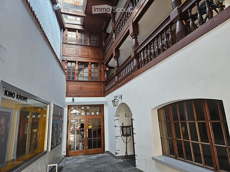 Grand hallway with wooden staircase, ornate balustrade, large windows, and decorative wall-mounted lamps.