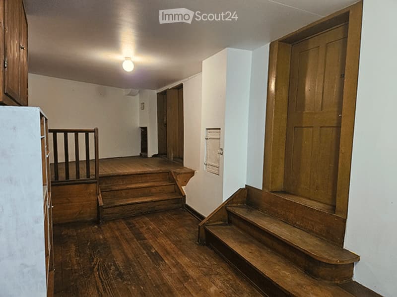 Empty wooden staircase and hallway with white walls, wooden railings, and a single light fixture on the ceiling.