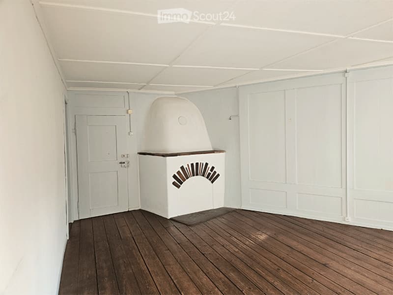 Completely empty room with white walls, wooden floor, and a single white door.