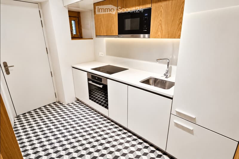 Modern kitchen with white cabinets, black and white geometric tiled floor, microwave, oven, sink, and faucet.