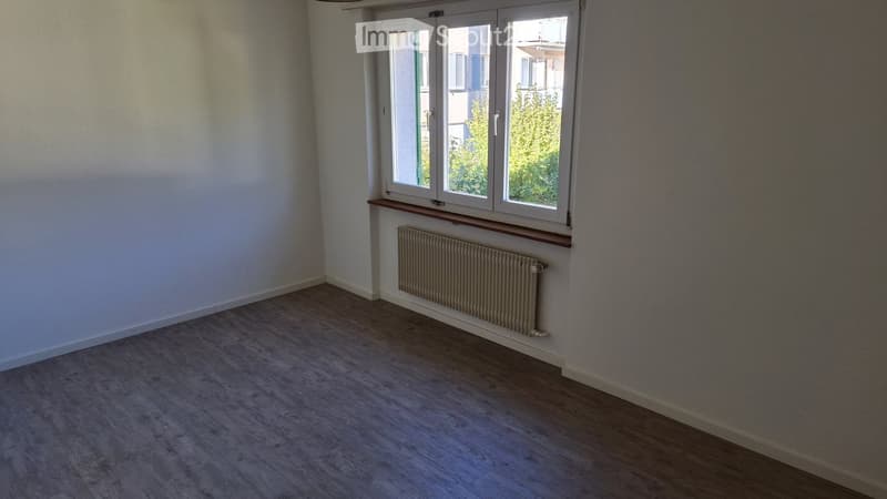 Empty room with wooden flooring, white walls, a radiator, and a window with a wooden sill.