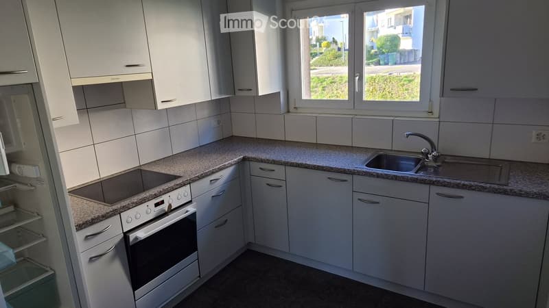 Modern kitchen with white cabinets, granite countertops, a sink, and an oven. Large windows provide natural light.