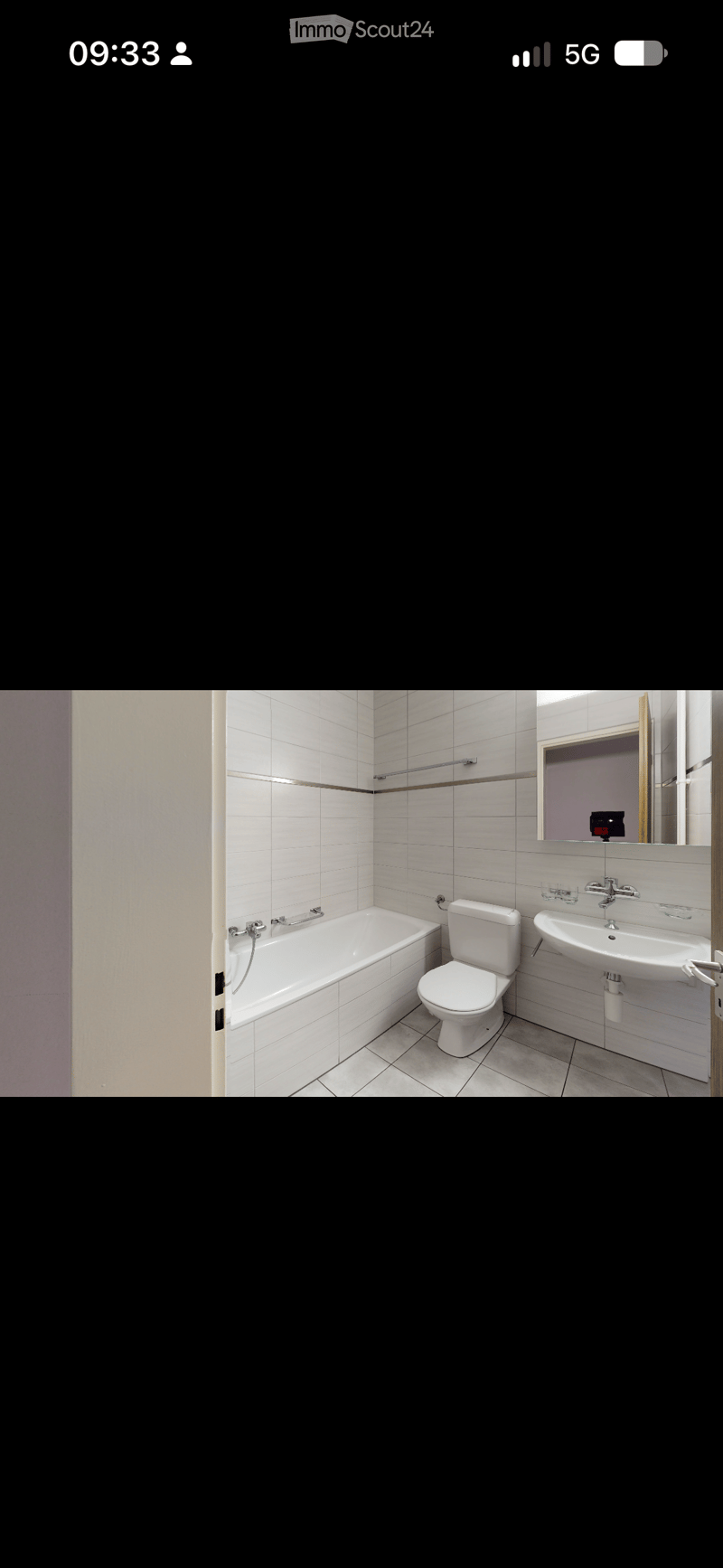 Modern bathroom with white tiles, bathtub, toilet, sink, and mirror.