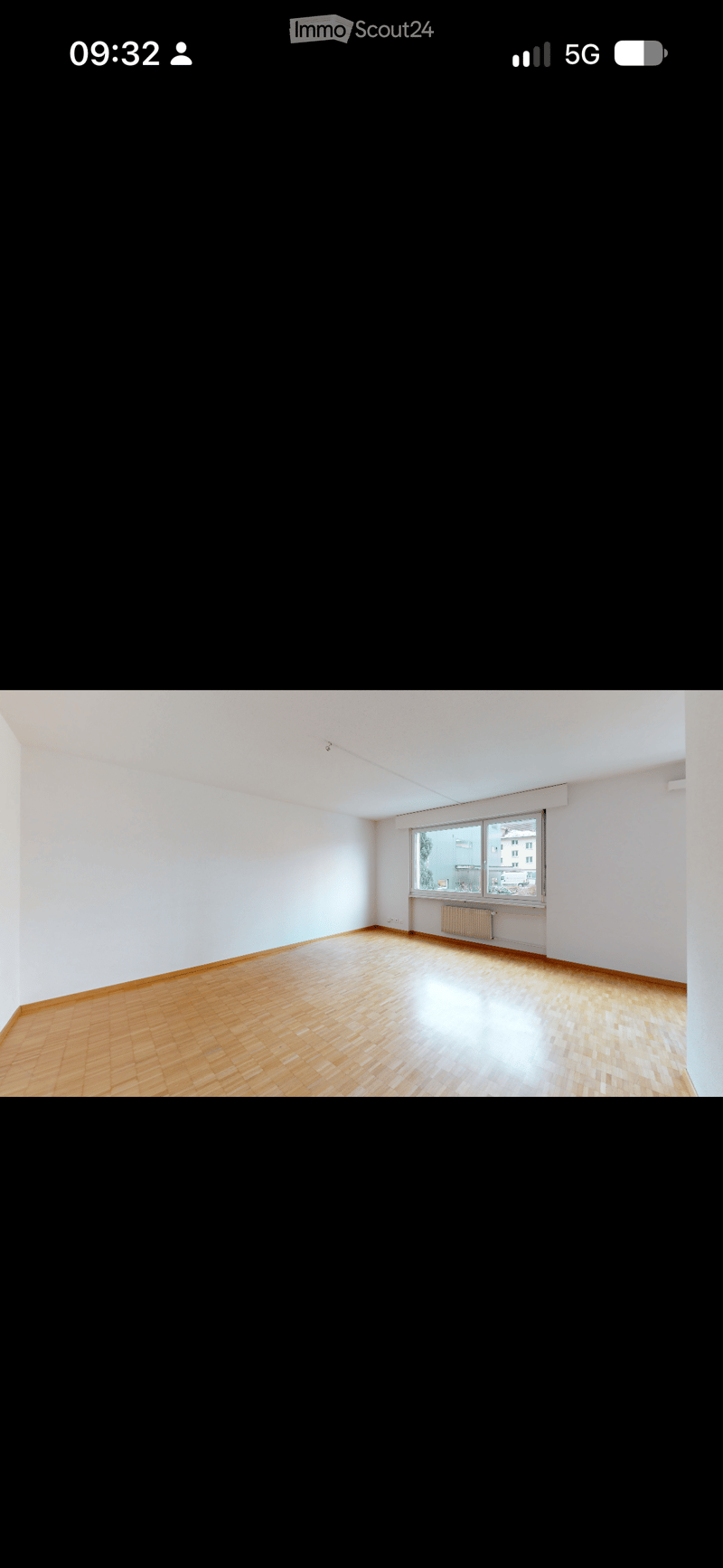 Empty room with wooden flooring, white walls, and a large window with a radiator below it.