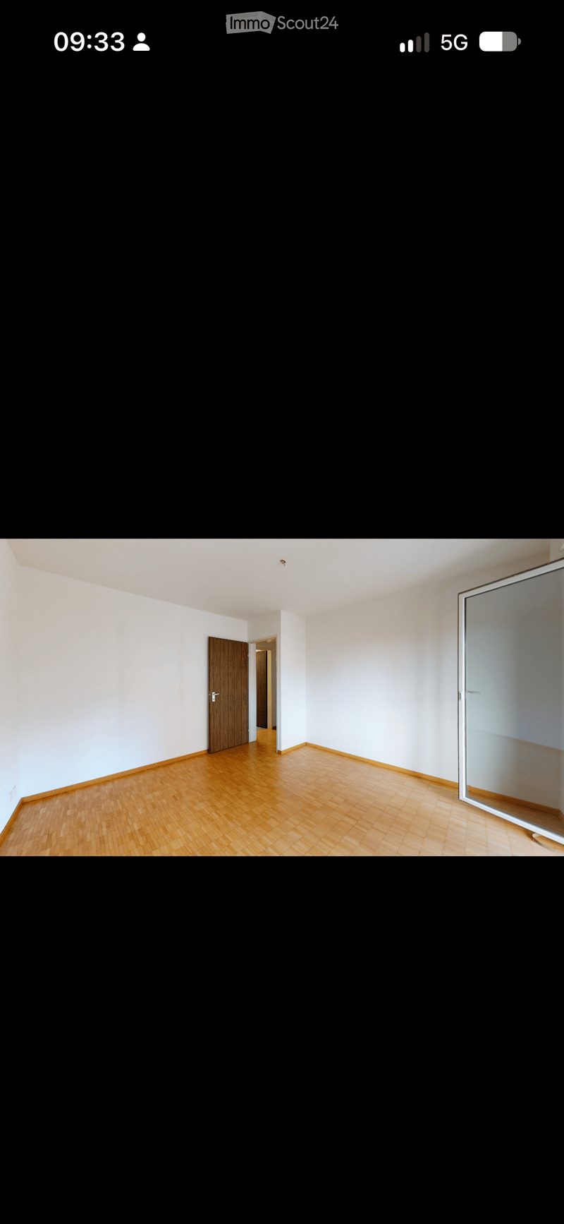 Empty room with wooden flooring, white walls, and a wooden door leading to another room.