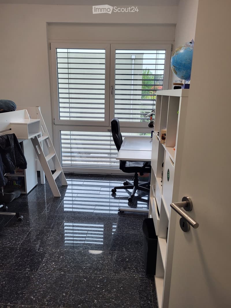 Office space with dark tiled floor, large window with blinds, desk, chair, globe, and shelves.