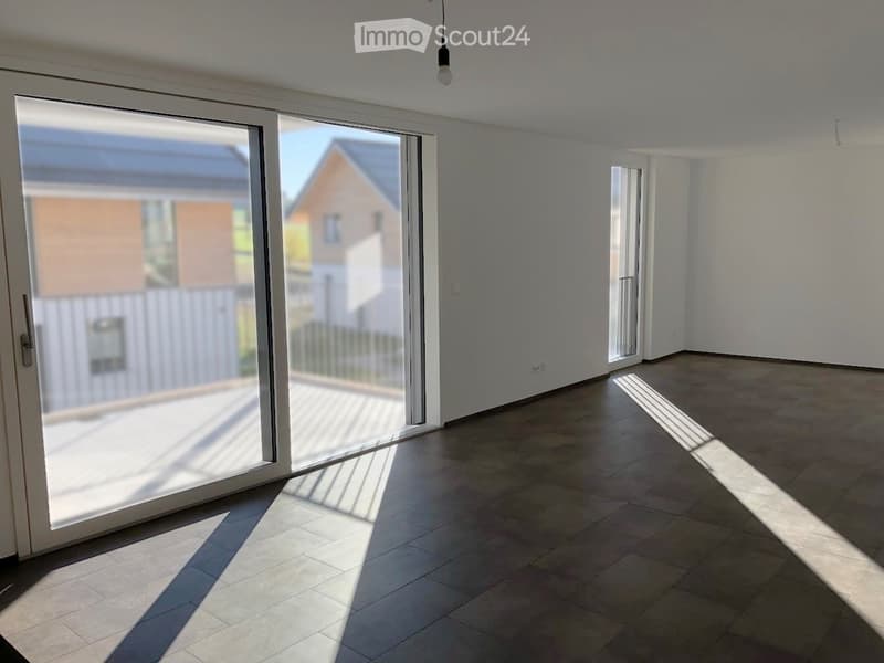Empty room with large sliding glass doors, tiled floor, and white walls. Sunlight streams in, casting shadows on the floor.