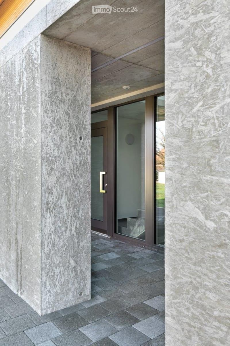 Modern building entrance with large stone pillars, glass doors, and a covered walkway.