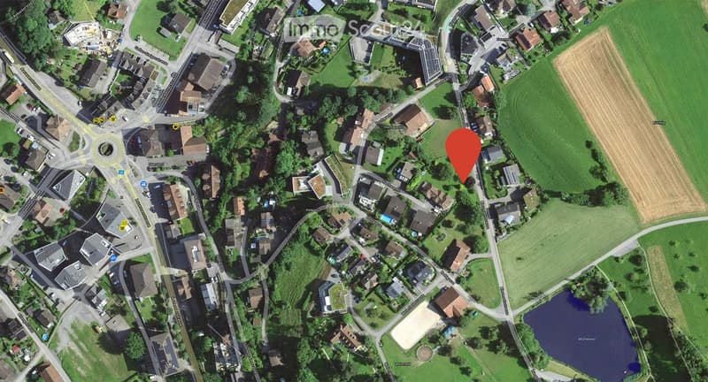 Aerial view of a residential area with houses, roads, and green spaces. The highlighted location is marked with a red pin.
