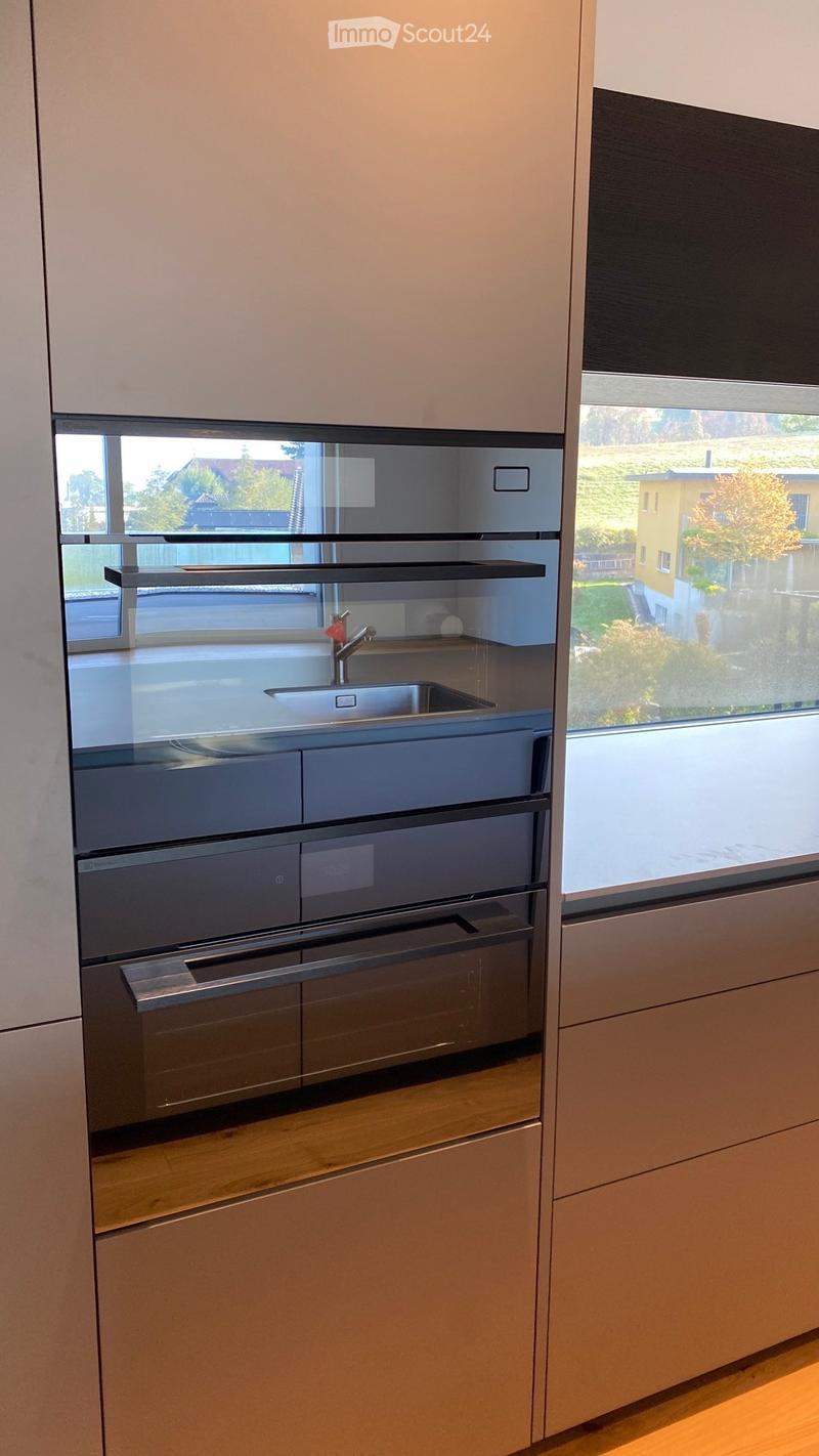 Modern kitchen with light-colored cabinets, stainless steel sink, and built-in oven. Large window offers a view of the outdoor area.