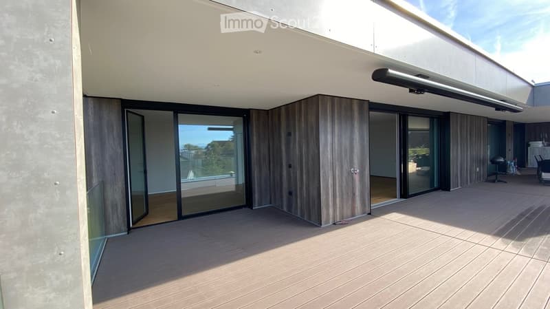 Modern outdoor deck with wooden flooring, large glass sliding doors leading to an indoor space, and a contemporary design with clean lines and a minimalist aesthetic.