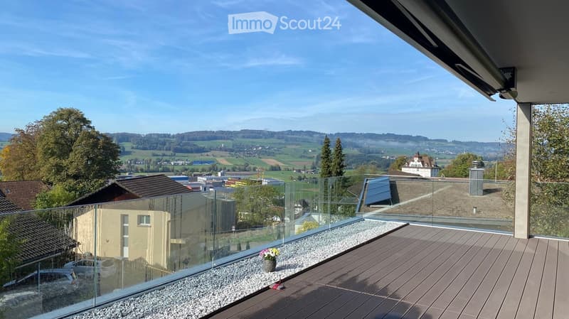 Modern balcony with wooden decking, glass railing, and scenic countryside view.