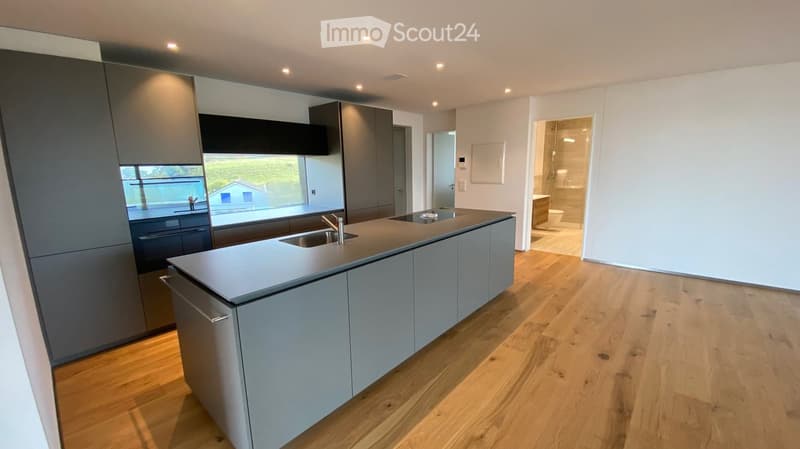 Modern kitchen with grey cabinets, a central island, and a sink. The space features wooden flooring and a view of the garden through a large window.