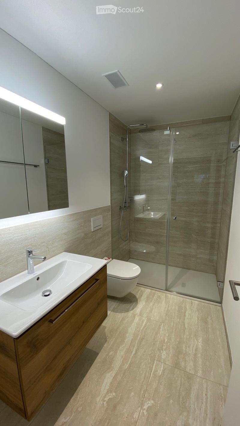 Modern bathroom with a white sink, wooden cabinet, toilet, glass-enclosed shower, and large mirror with built-in lighting.