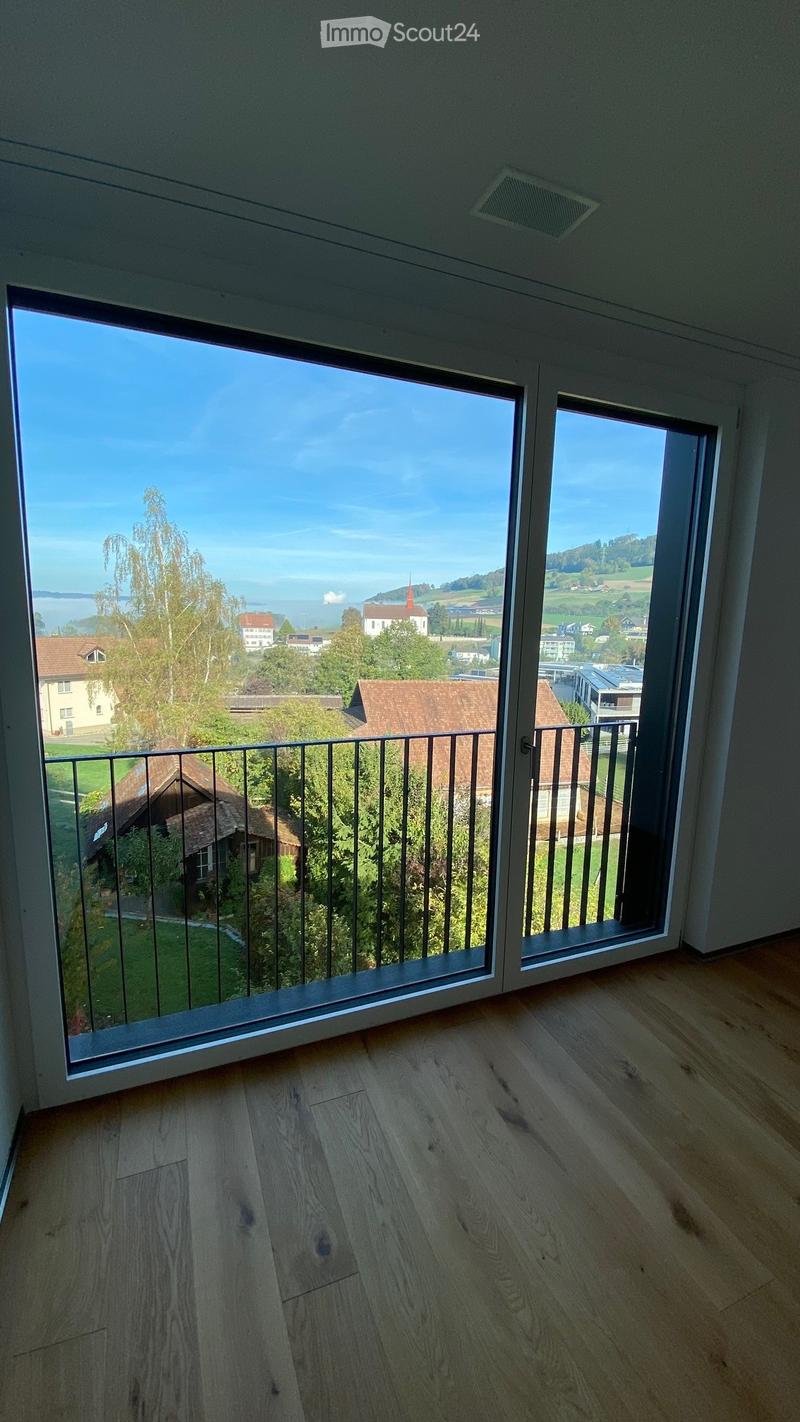 Empty balcony with wooden flooring and large glass doors opening to a scenic view of a town and landscape.