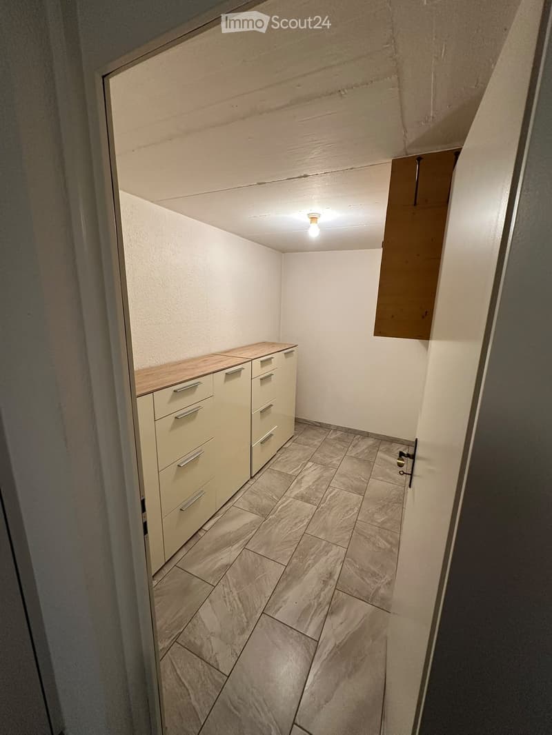 A narrow hallway with tiled flooring, white walls, and a small cabinet with drawers on one side.