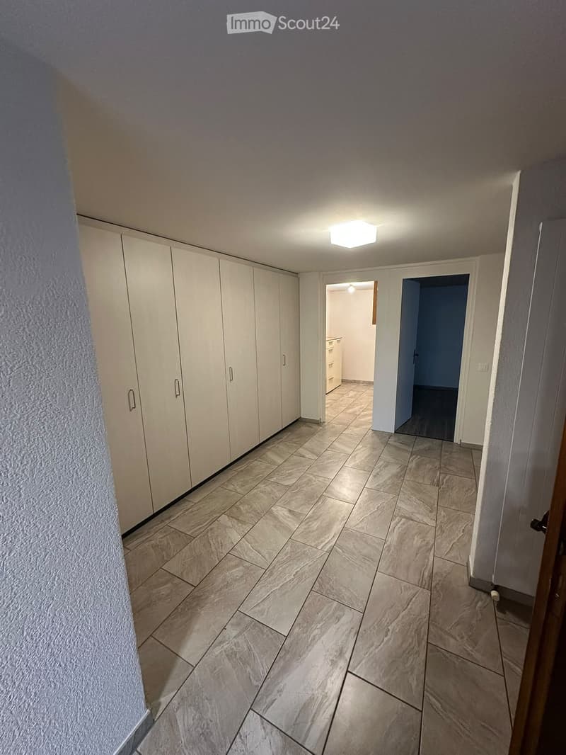 Empty hallway with tiled floor, white walls, built-in white closet units on one side, and two open doorways leading to other rooms.