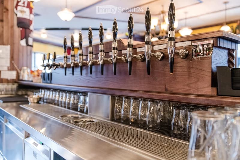 A bar counter with multiple beer taps and a row of empty glasses underneath.