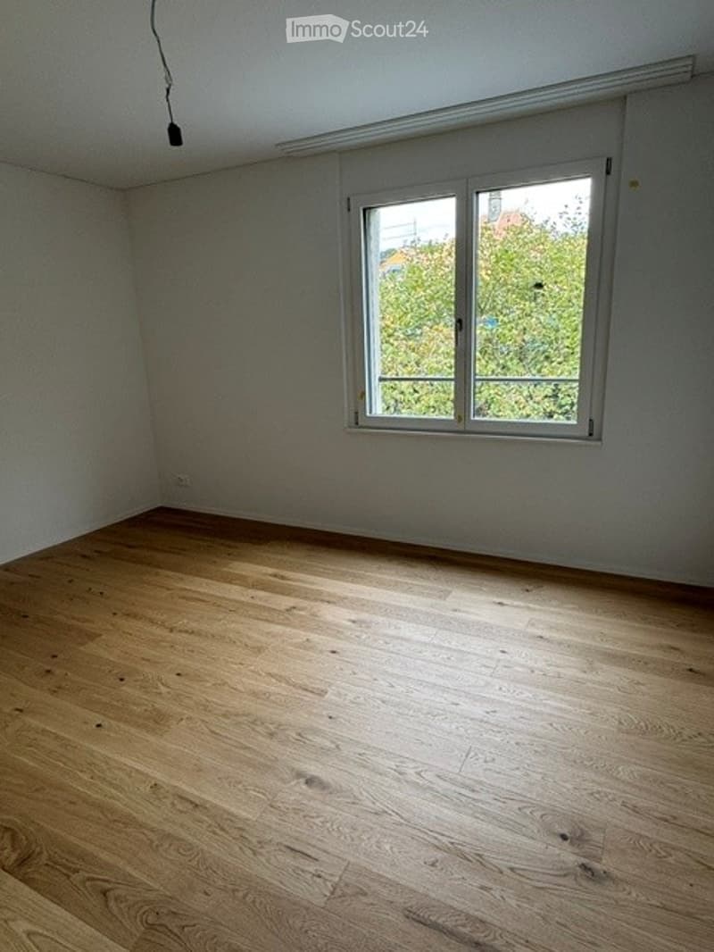 Empty room with wooden flooring and a large window letting in natural light. No furniture or equipment is present.