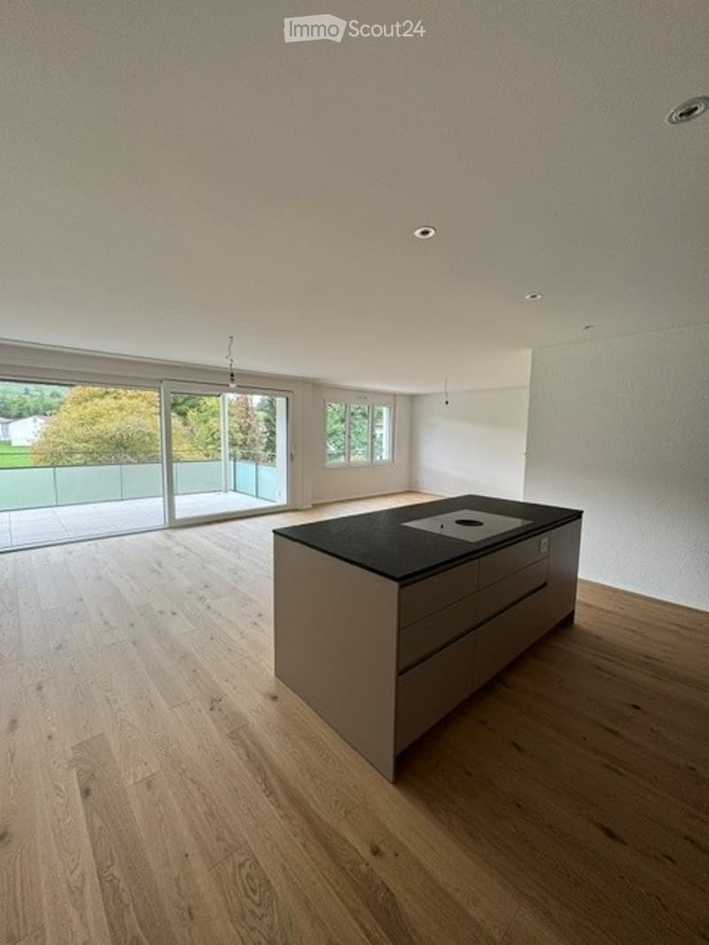 Empty kitchen with modern fitted units, black countertop, and large windows leading to a balcony.