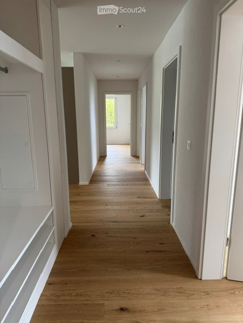 Empty hallway with light wooden flooring, white walls, and built-in shelving on one side.
