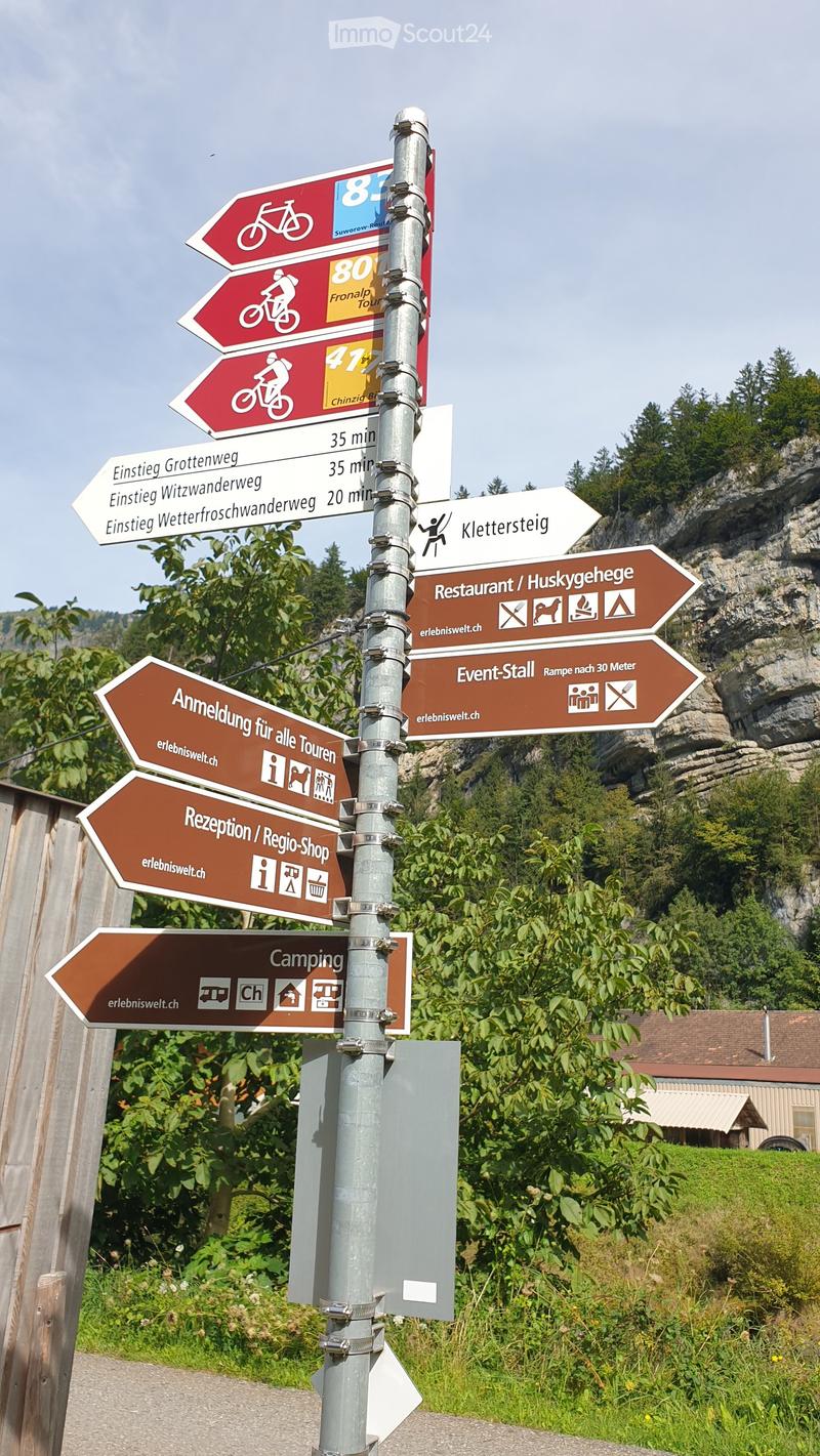 Directional signs mounted on a pole, pointing to various locations such as camping, reception, and restaurants, with surrounding greenery and a rocky hill in the background.