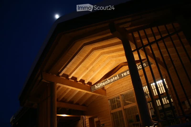 A wooden building with a slanted roof and illuminated signage reading "hüttenhotel_rez" at night.