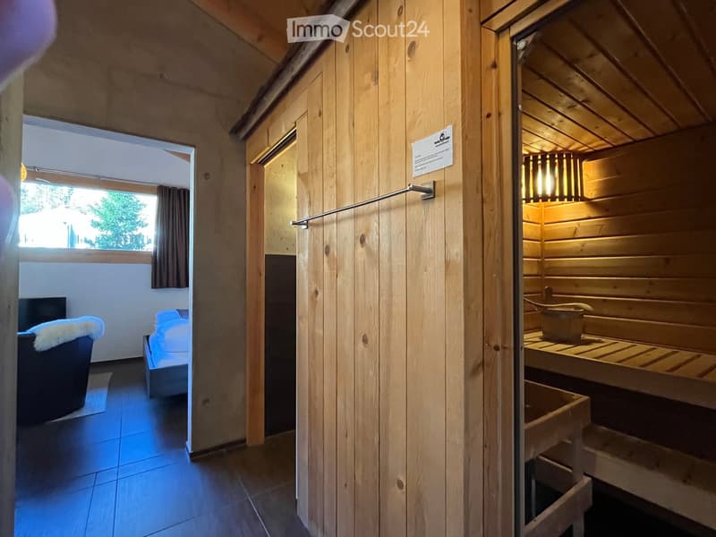 A cozy room with a bed, a sofa, and a wooden sauna area with benches, a lamp, and a bucket.