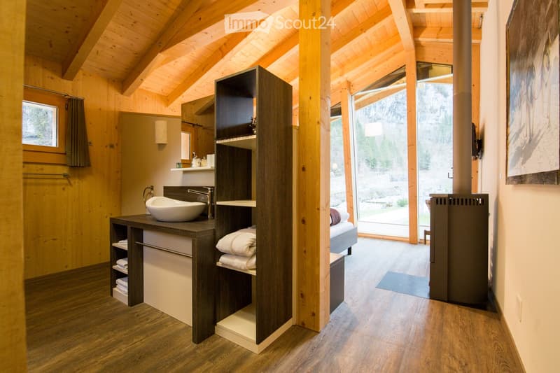 Modern bathroom with wooden beams, a sleek sink, towel rack, and large window overlooking a garden.