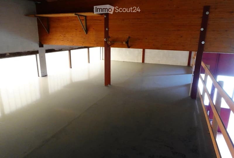 Empty room with polished concrete floor and wooden ceiling beams, featuring a staircase leading to an upper level.