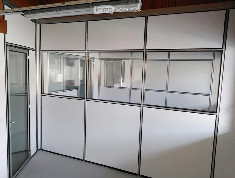 Empty room with white walls, grey carpet, and a large glass partition with frosted panels.