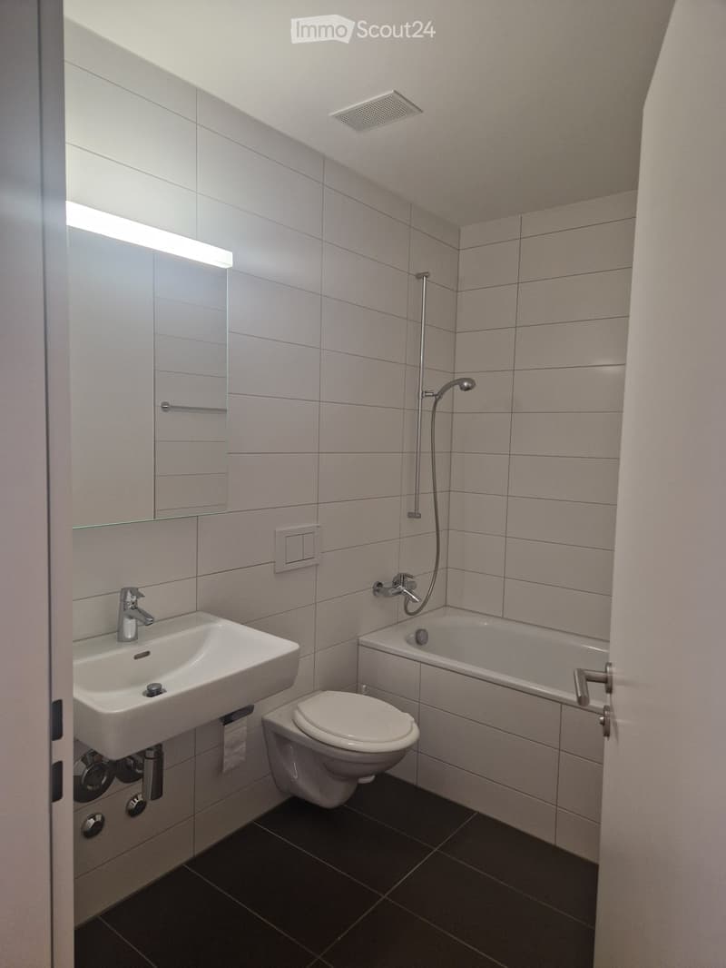 Modern bathroom with white tiles, a sink, toilet, bathtub, and a glass-enclosed shower area.