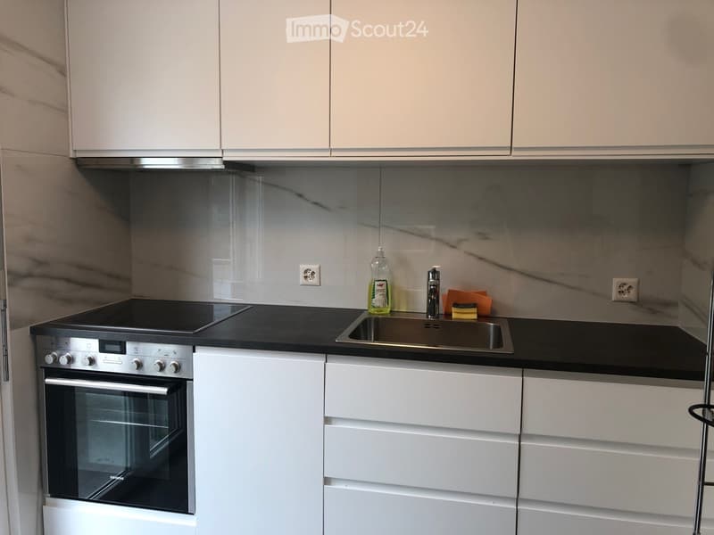Modern kitchen with white cabinets, black countertops, stainless steel sink, and built-in oven.