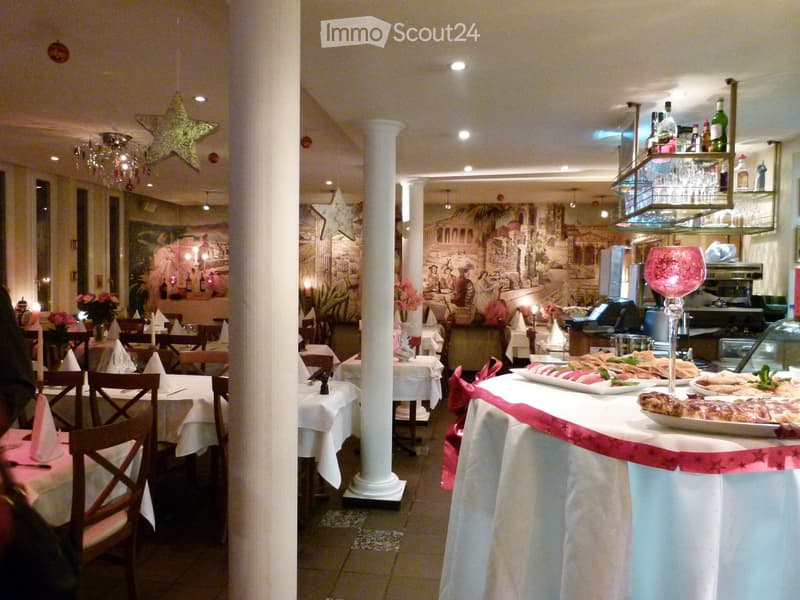 Restaurant interior with multiple tables and chairs, decorated with white tablecloths, napkins, and a buffet table with food and drinks.