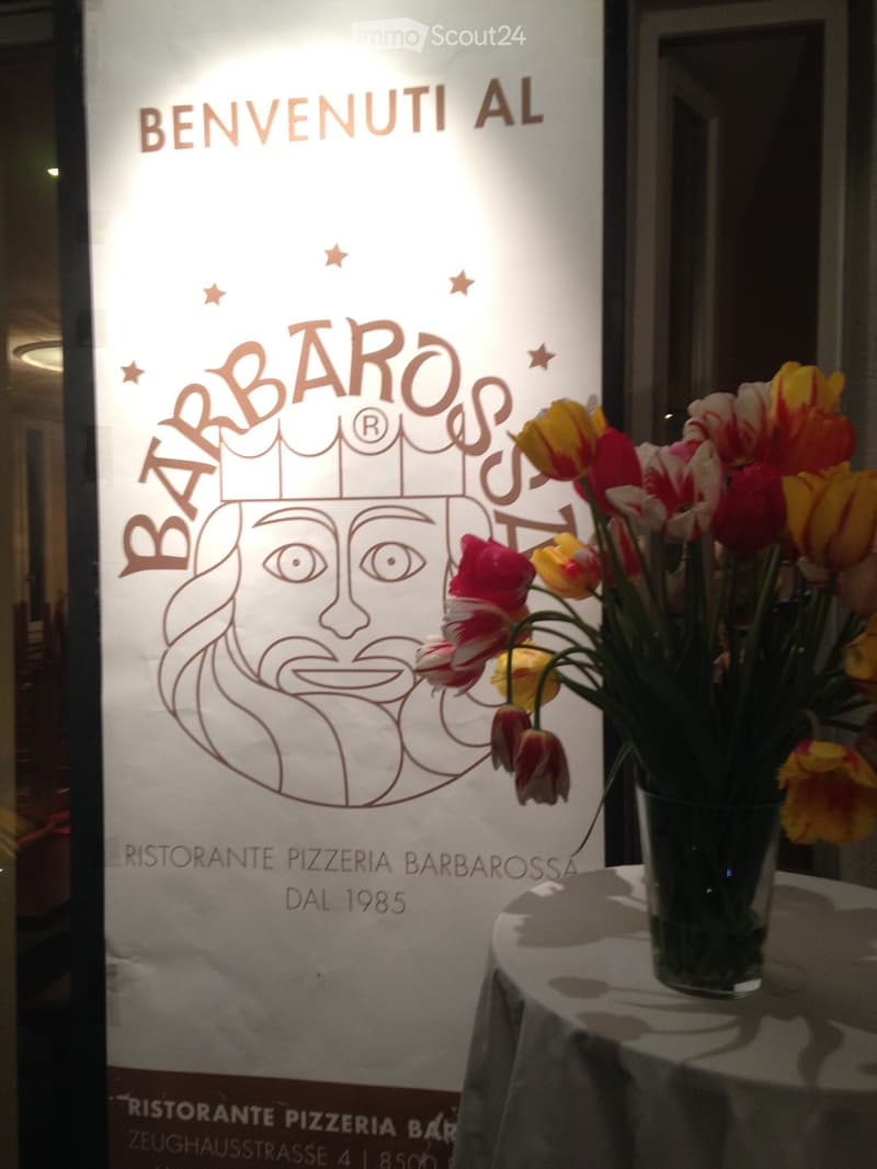 A restaurant entrance with a decorative sign reading "Benvenuti al Barbaresi" and a vase of colorful tulips on a table.