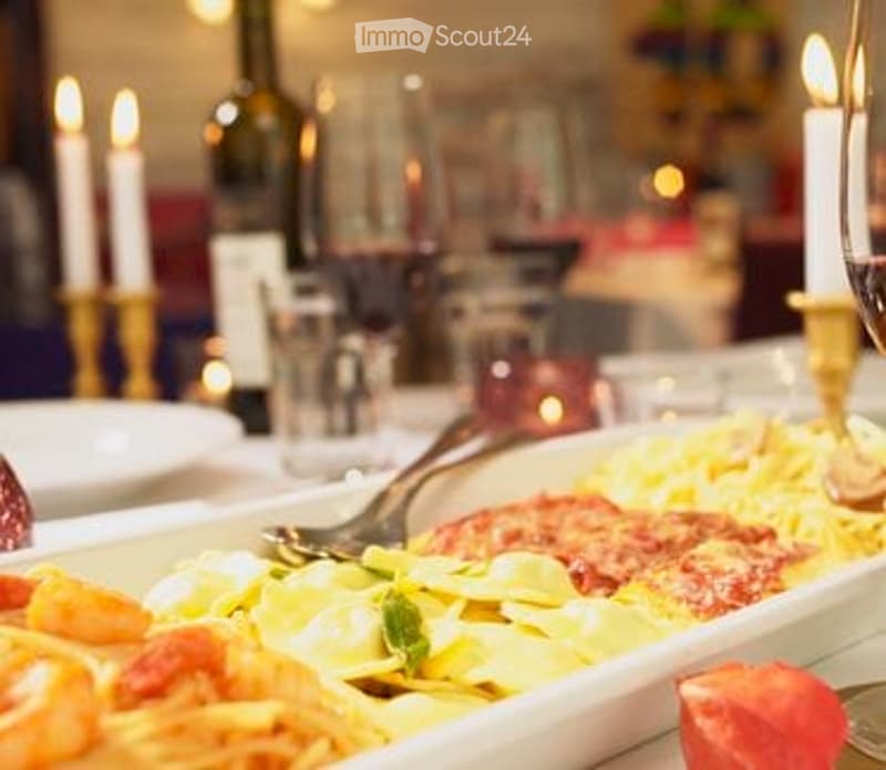 A beautifully arranged dining table with a pasta dish, wine bottle, wine glass, and lit candles, creating a warm and inviting atmosphere.